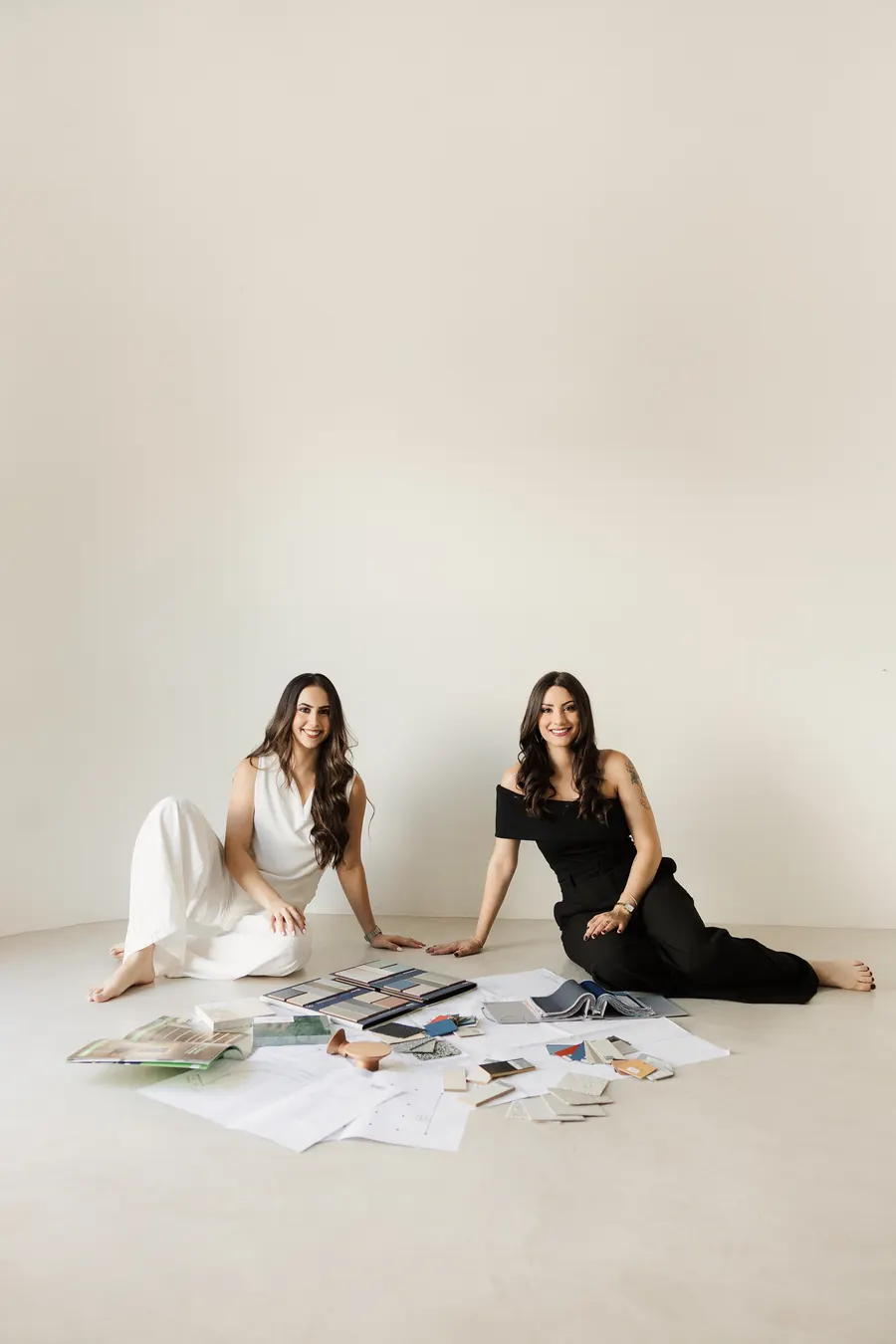 Malu e Laura, arquitetas do Studio Óri, sentadas no chão com amostras de materiais e plantas de projeto